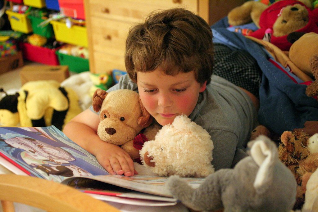 Niño leyendo un libro rodeado de peluches