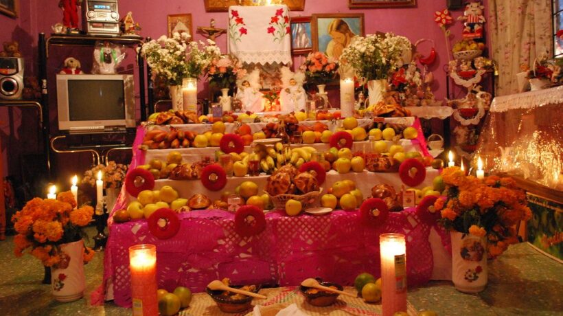 Ofrenda casera de Día de Muertos con cempasúchil, fruta, pan y velas encendidas