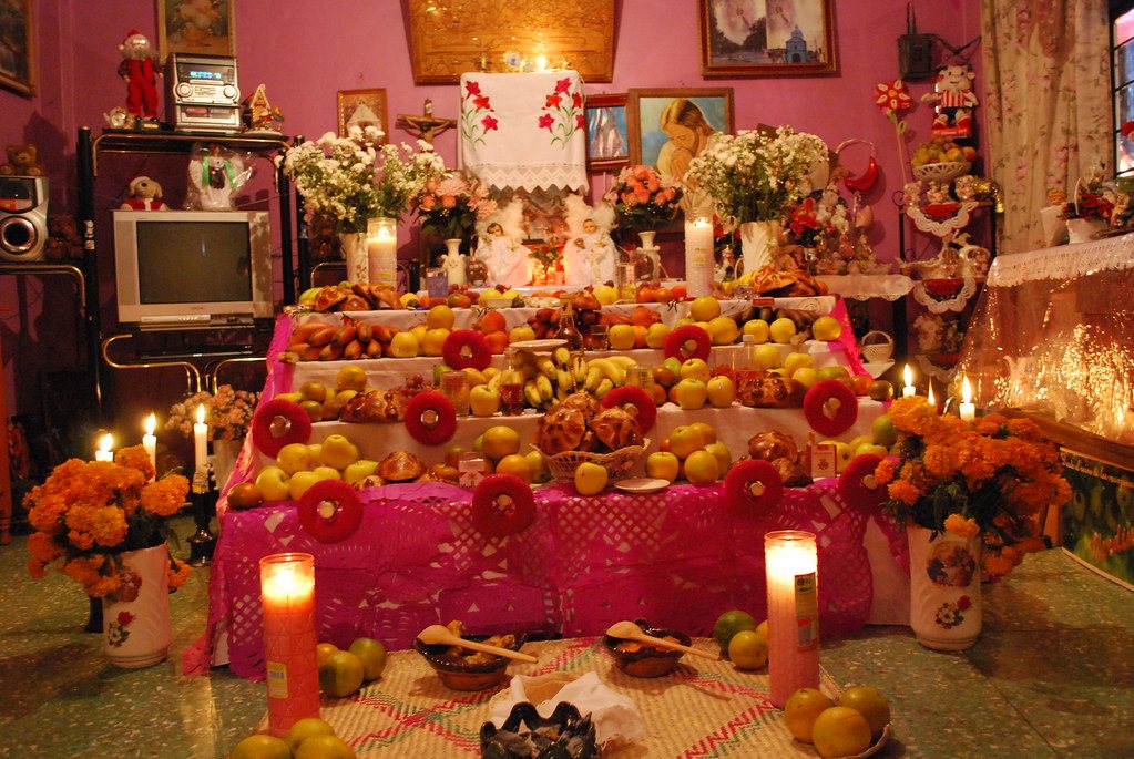 Ofrenda casera de Día de Muertos con cempasúchil, fruta, pan y velas encendidas